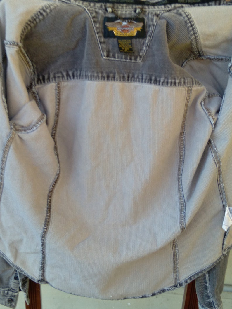May include: A gray denim jacket with a Harley Davidson logo on the back. The jacket is unzipped and the lining is visible.