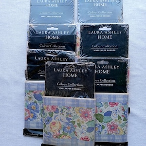 May include: A collection of Laura Ashley Home wallpaper borders. The packages are in various sizes and feature floral and plaid patterns in shades of blue, pink, and white. The text "Colour Collection" and "Wallpaper Border" are visible on the packaging.
