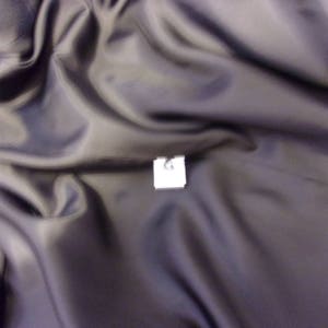 May include: A close-up of a dark gray fabric with a white tag that says "L" on it.