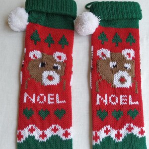 May include: Two red Christmas stockings with green cuffs and white pom-poms. Each stocking features a brown reindeer design, green Christmas trees, and the word "NOEL" in white. White and green patterns decorate the bottom.
