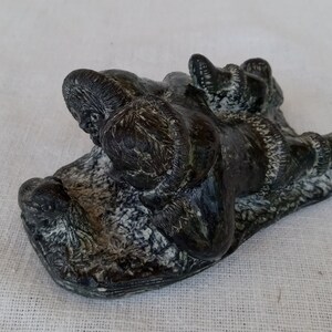 May include: A black and white soapstone sculpture of two people on a sled. The sculpture is carved in a realistic style and shows the people in a relaxed pose.