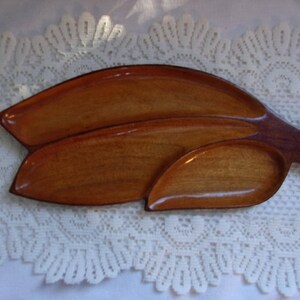 May include: A wooden serving tray with three sections, shaped like a leaf. The tray is made of light brown wood and has a natural finish.