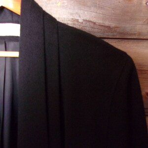 May include: A black long-sleeved jacket with a shawl collar. The jacket is made of a soft, smooth fabric.