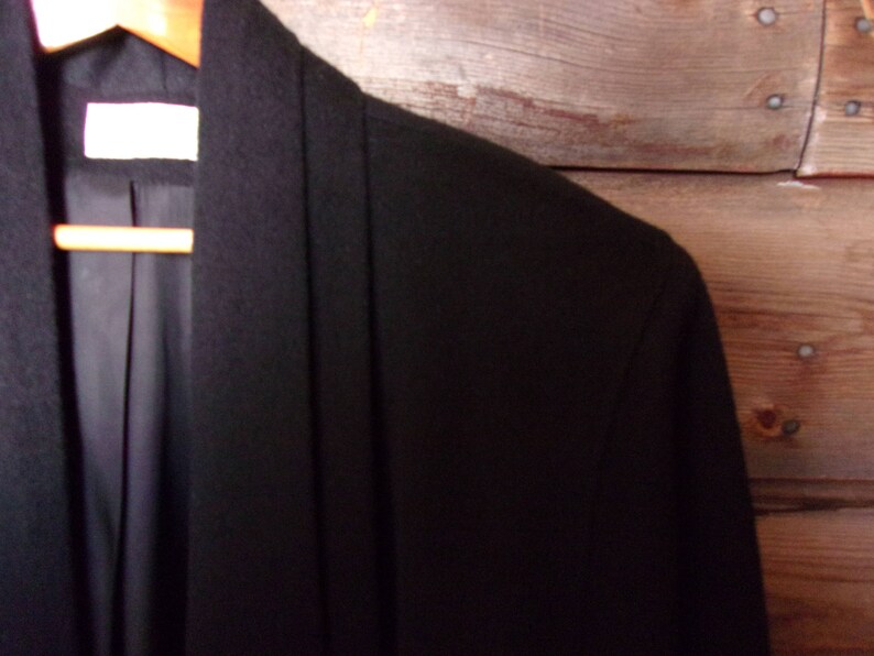 May include: A black long-sleeved jacket with a shawl collar. The jacket is made of a soft, smooth fabric.