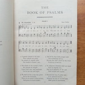 May include: An open book page titled The Book of Psalms, displaying Psalm 1 with musical notation for St. Flavian. The text includes the lyrics O greatly blessed is the man who walketh not astray, printed in black ink on an off-white paper page.