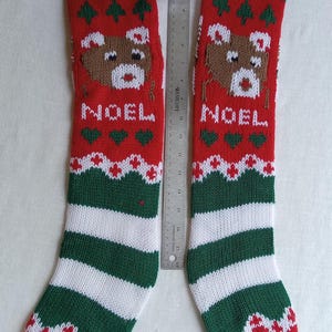 May include: Two red and green Christmas stockings with a reindeer design and the word "NOEL". The stockings have white pom-poms and green and white striped bottoms. The stockings are approximately 18 inches long.