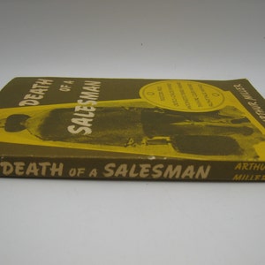 May include: A yellow and brown paperback book titled "Death of a Salesman" by Arthur Miller. The cover features a black and white photo of a man in a suit.