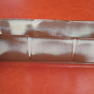 May include: A brown and white glazed ceramic planter with a rectangular shape. The planter has a slightly rounded bottom and a smooth, glossy finish.