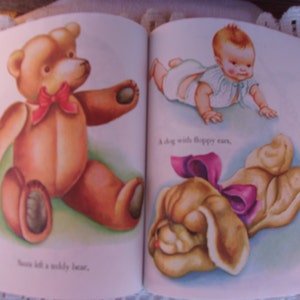 May include: A vintage children's book spread featuring illustrations. One page shows a brown teddy bear with a red bow. The opposite page depicts a baby and a dog with floppy ears, also with a pink bow. Text is included.
