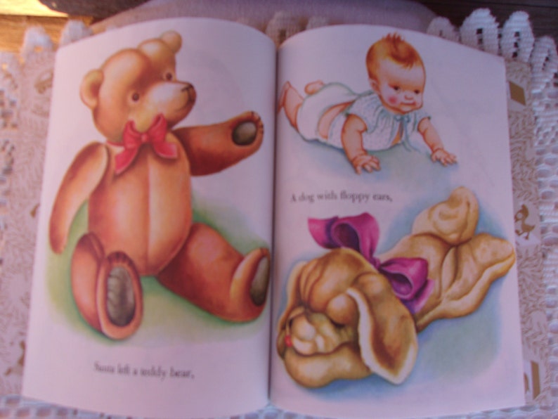 May include: A vintage children's book spread featuring illustrations. One page shows a brown teddy bear with a red bow. The opposite page depicts a baby and a dog with floppy ears, also with a pink bow. Text is included.