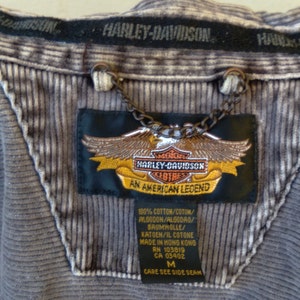 May include: A gray corduroy jacket with a Harley-Davidson logo patch. The patch features an eagle with a shield that says "Harley-Davidson Clothes An American Legend". The tag also says "100% Cotton/Coton/Algodon/Algodao/Baumwolle/Katoen/Il Cotone Made in Hong Kong RN 103819 CA 03402 M Care See Side Seam".