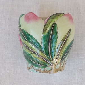 Puede incluir: Un jarrón de cerámica con forma de corazón con un diseño de hojas verdes y doradas y detalles en rosa.