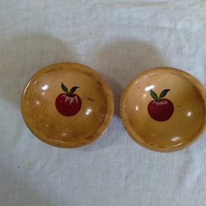 May include: Two small wooden bowls with a painted red apple design. The bowls are light brown with a natural wood grain.