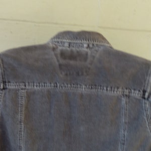 May include: A gray corduroy jacket with a zipper closure and a small label on the back.