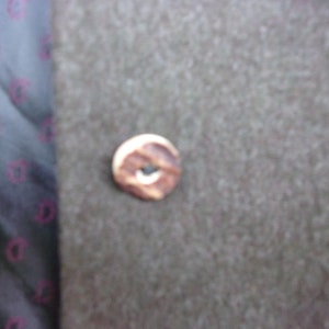 May include: Close-up of a brown button with a light-colored edge and a dark center. The button is on a textured, gray fabric. A patterned fabric with a dark background and pink designs is visible on the left.