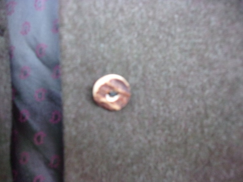 May include: Close-up of a brown button with a light-colored edge and a dark center. The button is on a textured, gray fabric. A patterned fabric with a dark background and pink designs is visible on the left.