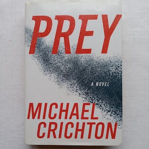 May include: A white book cover with the title "PREY" in red letters. The author's name, "MICHAEL CRICHTON", is also in red letters. The book cover has a black and white splatter design.