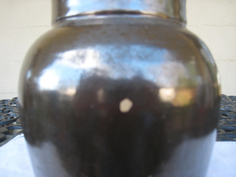 May include: A dark brown ceramic crock with a smooth, glossy finish. The crock has a slight indentation on the side.