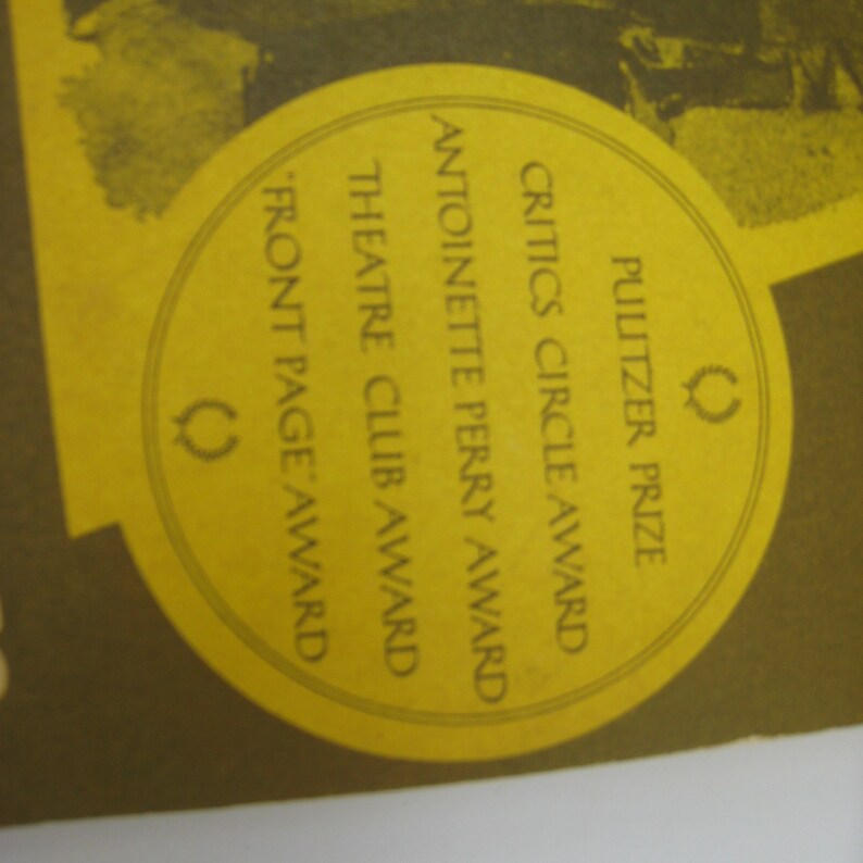 May include: A yellow circle with the text "Pulitzer Prize", "Critics Circle Award", "Antoinette Perry Award", "Theatre Club Award", and "Front Page Award" in black text. A laurel wreath symbol is on the right side of the circle.
