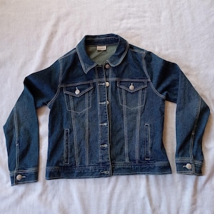 May include: A dark blue denim jacket with a button closure, two chest pockets, and two front pockets.