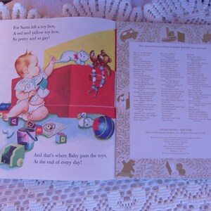 May include: Open book illustration featuring a baby with toys. Text reads, "For Santa left a toy box, A red and yellow toy box, So pretty and so gay!" and "And that's where Baby puts the toys, At the end of every day!"