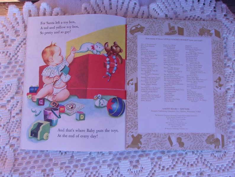 May include: Open book illustration featuring a baby with toys. Text reads, "For Santa left a toy box, A red and yellow toy box, So pretty and so gay!" and "And that's where Baby puts the toys, At the end of every day!"