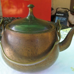 May include: A brass teapot with a green lid and a decorative handle. The teapot has an ornate design etched into the metal.