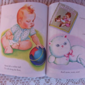 May include: A vintage children's book illustration featuring a baby, a rubber ball, and a fluffy white cat with a pink bow. The book is open, displaying colorful images and text. The baby is reaching for the ball.