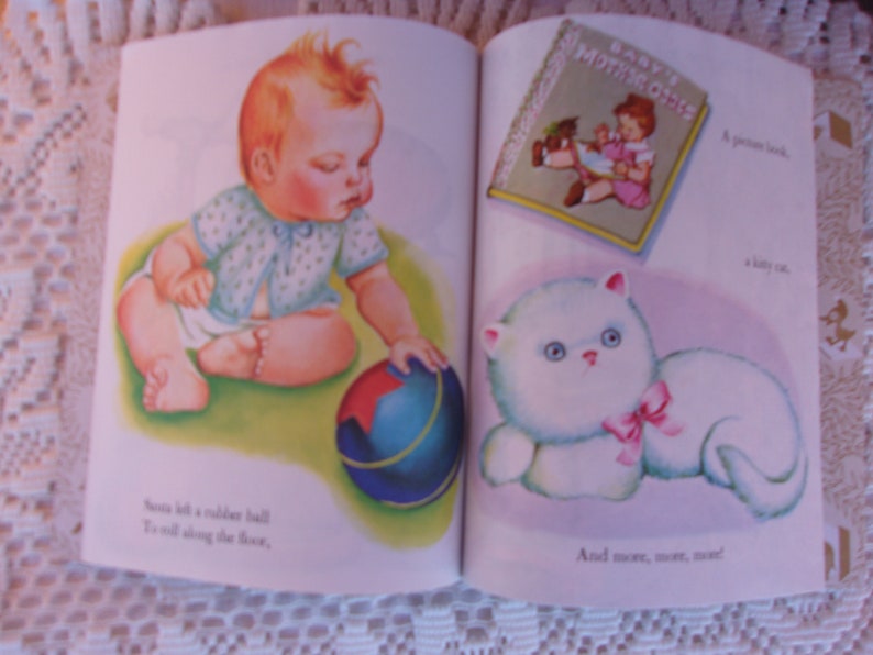 May include: A vintage children's book illustration featuring a baby, a rubber ball, and a fluffy white cat with a pink bow. The book is open, displaying colorful images and text. The baby is reaching for the ball.