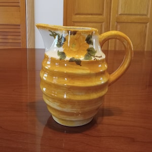 May include: A yellow ceramic pitcher with a white rim and floral design. The pitcher has a ribbed texture and a handle.
