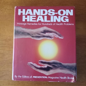 May include: A red book titled "HANDS-ON HEALING" with the subtitle "Massage Remedies for Hundreds of Health Problems." The cover features two hands cupping a yellow sun. The book is by the Editors of PREVENTION Magazine Health Books.