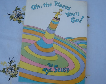 May include: A colorful book cover with the title "Oh, the Places You'll Go!" by Dr. Seuss. The cover features a yellow figure standing on a striped, swirling, multi-colored structure.