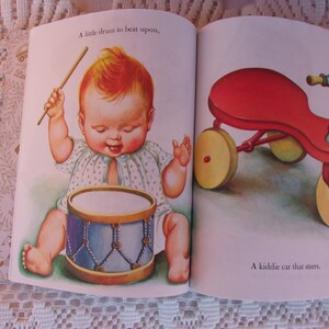 May include: Illustration from a children's book featuring a baby playing a drum and a red tricycle. The baby is depicted with rosy cheeks and a happy expression, holding drumsticks. The tricycle has yellow wheels.