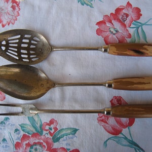 May include: Three vintage kitchen utensils with wooden handles. A slotted spoon, a solid spoon, and a fork.