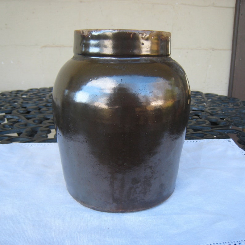May include: A large, dark brown glazed stoneware crock with a rounded body and a wide mouth.
