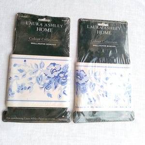 May include: Two rolls of Laura Ashley Home wallpaper border. The border features a floral design in shades of blue on a cream background. The packaging includes the text "Colour Collection" and "Wallpaper Border".