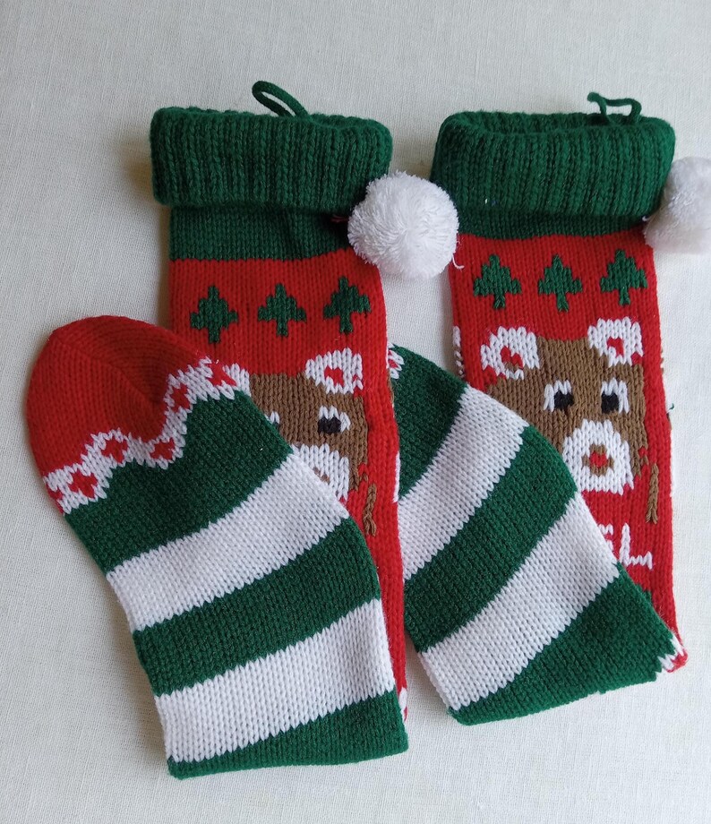 May include: Christmas stockings and matching mittens. The stockings are red with a reindeer and tree pattern, green cuffs, and white pom-poms. The mittens are red with a white and green striped pattern.