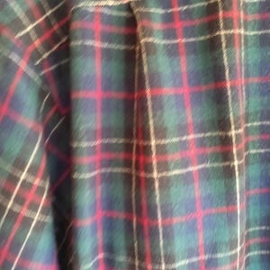 May include: A long-sleeved button-down shirt featuring a classic plaid pattern. The fabric displays a repeating grid design composed of deep forest green, navy blue, and black squares, accented by thin, vibrant red and off-white vertical and horizontal lines.