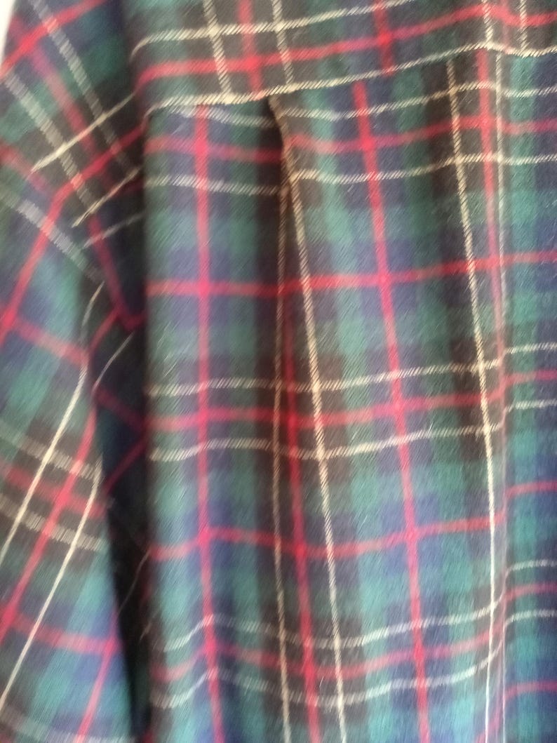 May include: A long-sleeved button-down shirt featuring a classic plaid pattern. The fabric displays a repeating grid design composed of deep forest green, navy blue, and black squares, accented by thin, vibrant red and off-white vertical and horizontal lines.