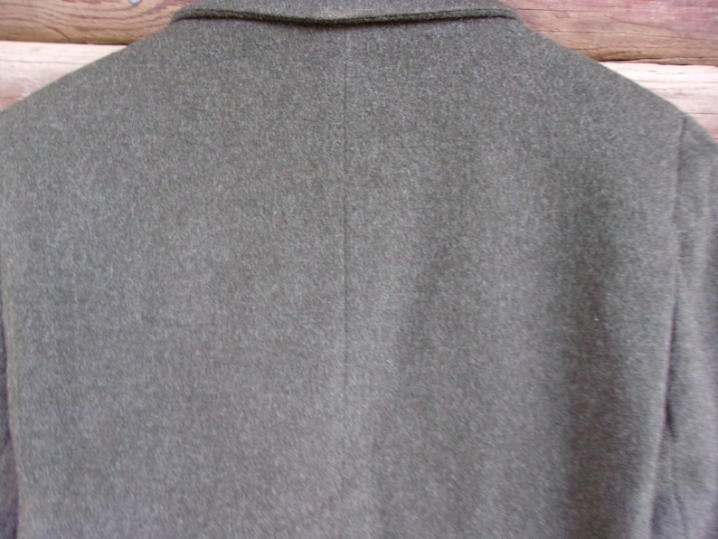 May include: Close-up of the back of a gray wool blazer. The blazer has a notched collar and a center back seam. The fabric has a slightly textured appearance. The background is a wooden surface.