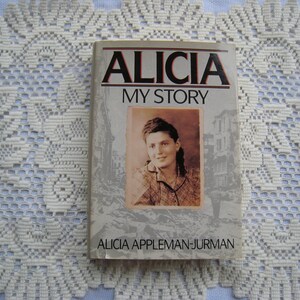May include: A book titled "Alicia My Story" by Alicia Appleman-Jurman. The cover features a black and white photo of a woman with dark hair and a light-colored shirt. The background of the photo appears to be a city street.