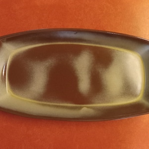 May include: Rectangular serving platter with a brown and tan gradient glaze. The ceramic dish has rounded corners and a slightly raised edge. The interior is a lighter tan color, transitioning to a darker brown around the edges.