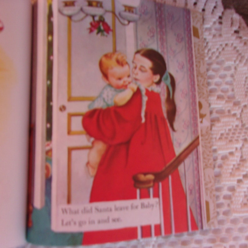May include: Illustration from a children's book featuring a young girl in a red dress holding a baby. The baby is wearing a light blue outfit. The text at the bottom reads, "What did Santa leave for Baby? Let's go in and see."
