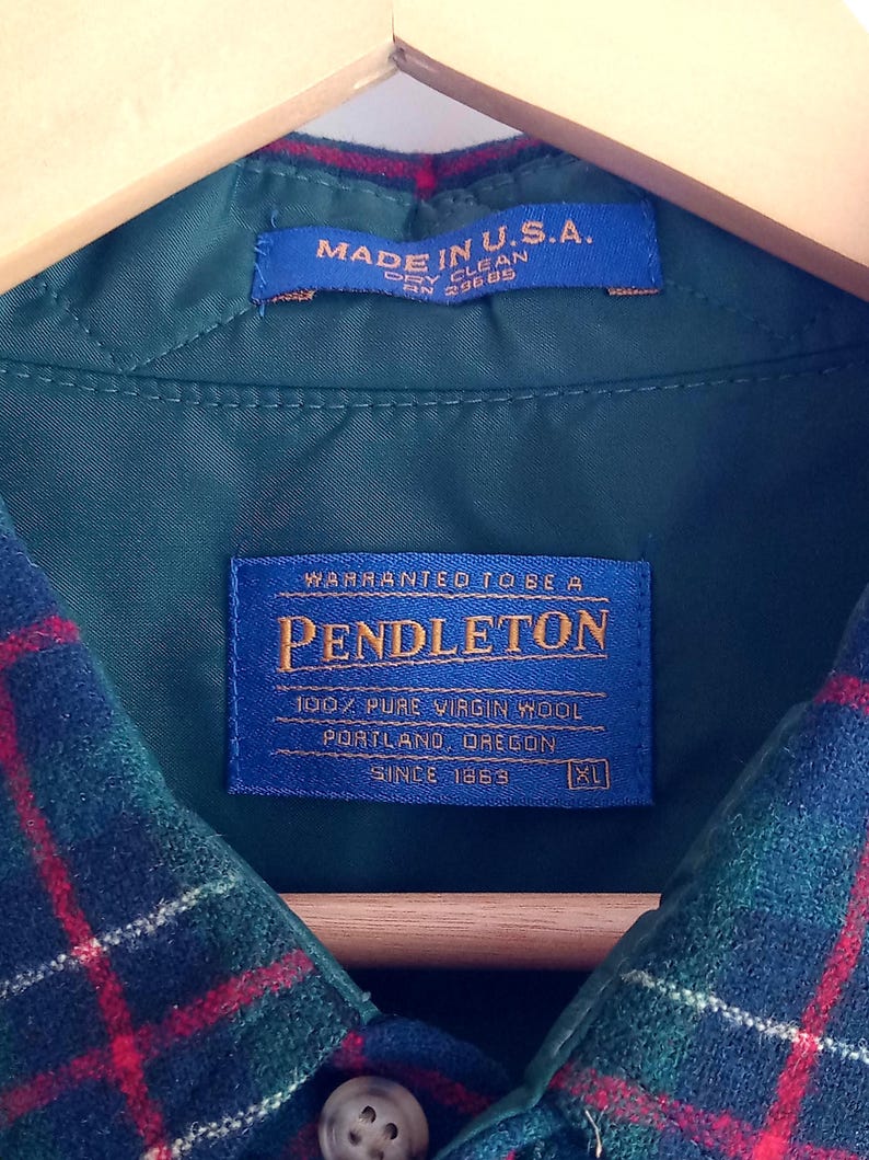 May include: A green plaid wool shirt with a blue interior label reading Warranted To Be A Pendleton 100% Pure Virgin Wool Portland Oregon Since 1863 XL and a secondary blue label stating Made In U.S.A. Dry Clean RN 29685, featuring a button closure.