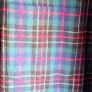 May include: A textile fabric featuring a classic plaid pattern with intersecting lines in shades of dark green, navy blue, and black, accented by thin, vibrant red and white horizontal and vertical stripes throughout the woven material.