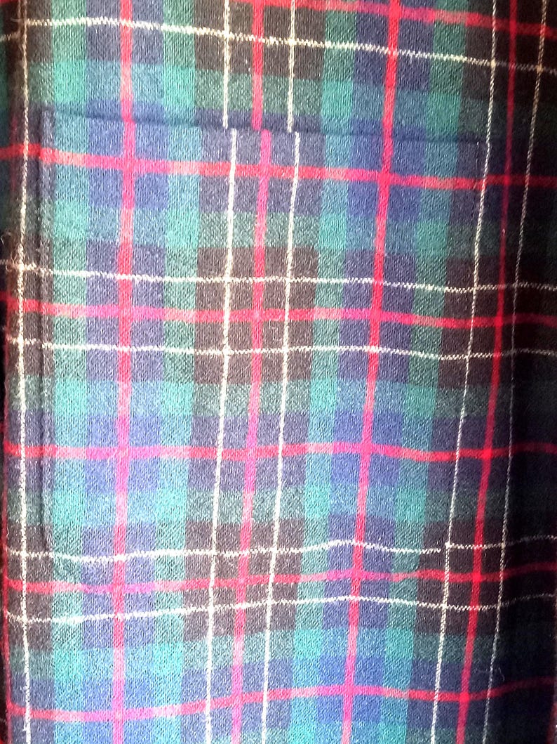 May include: A textile fabric featuring a classic plaid pattern with intersecting lines in shades of dark green, navy blue, and black, accented by thin, vibrant red and white horizontal and vertical stripes throughout the woven material.