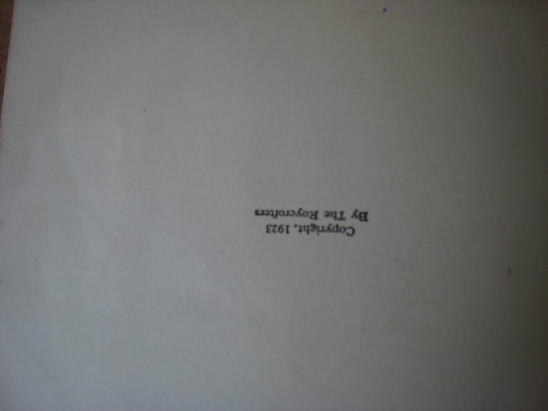 May include: A white page featuring black printed text oriented vertically. The text reads Copyright, 1923 By The Roycrofters. The paper surface appears smooth and matte, with a subtle crease visible running diagonally across the lower section.