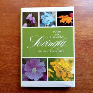 May include: A paperback book titled "Lovingly" by Helen Steiner Rice. The cover features a green banner with the title and author's name, and four floral images. The book is set against a wooden background.