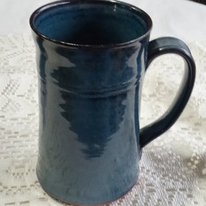 May include: A teal blue ceramic mug with a rounded handle. The mug has a slightly flared rim and a smooth, glossy finish.