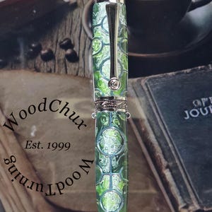 Może przedstawiać: Ręcznie wykonane pi&oacute;ro z zielono-białym wzorem na korpusie, zaakcentowane srebrnymi metalowymi detalami. Pi&oacute;ro posiada ozdobny klips i kryształową ozdobę. Pi&oacute;ro od WoodChux, Est. 1999.